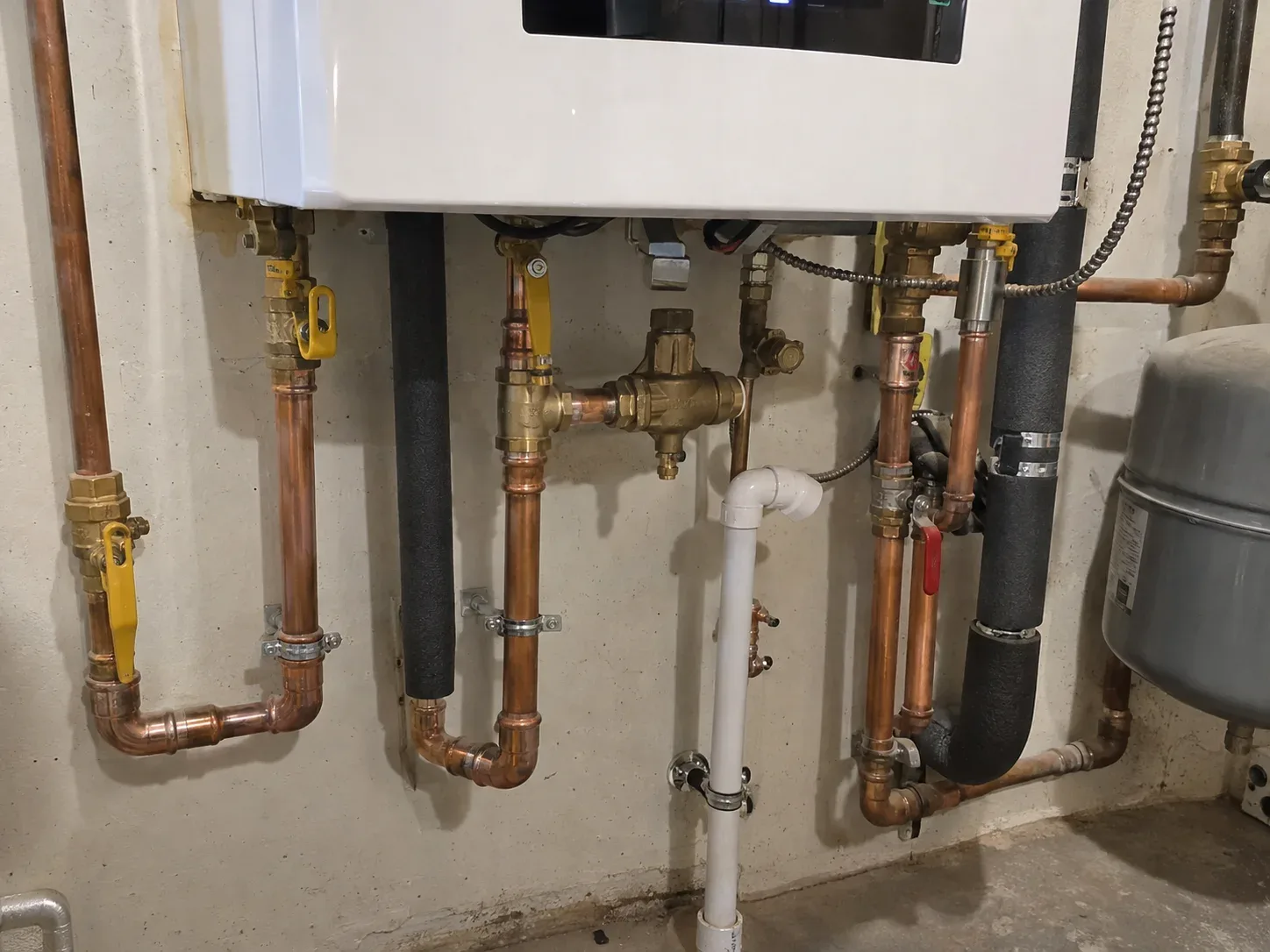 Finished wall-mounted boiler installation with neatly arranged and labelled pipes